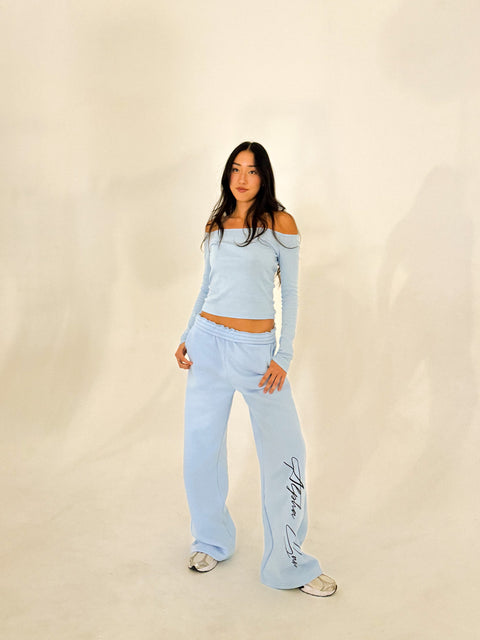 Woman wearing a light blue outfit with 'Alpha Gam' branding on a beige background